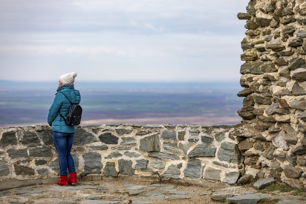 a woman in a blue jacket standing on a stone wall