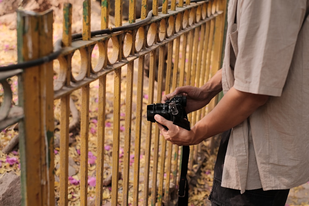 a man holding a camera standing next to a fence