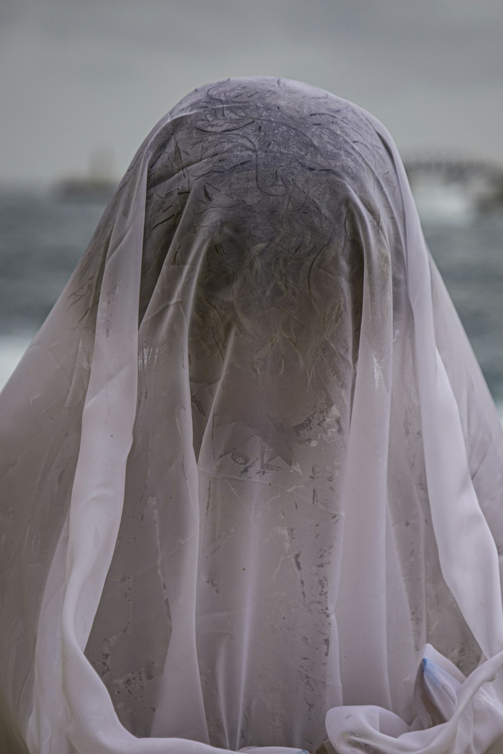 a woman covered in a white veil standing in front of a body of water