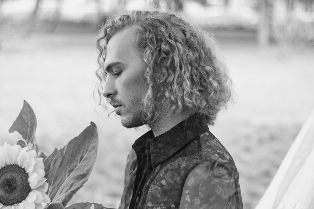 a man with curly hair holding a sunflower