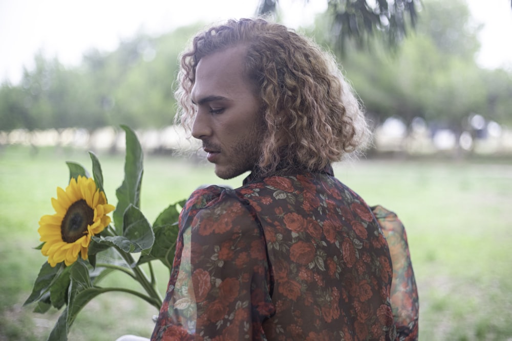 a man with curly hair holding a sunflower