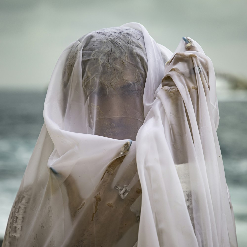 a woman with a veil on her head standing in front of the ocean