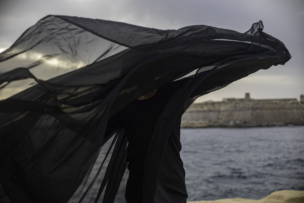 a woman in a black dress is standing by the water