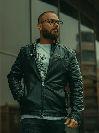 A stylish man wearing a sleek black jacket with red accents, standing confidently in an urban setting.