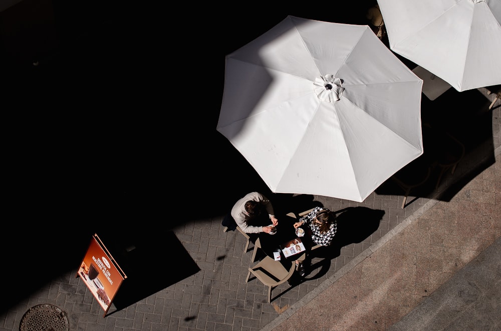 an overhead view of two people sitting at a table with umbrellas
