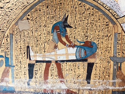 An ancient Egyptian art piece depicting Anubis, the jackal-headed god, performing a ritual on a mummified figure. Hieroglyphics fill the background, adding to the historical and cultural context.