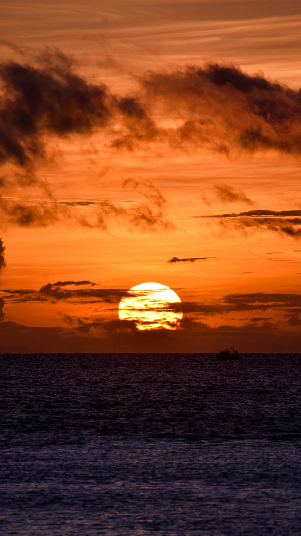 the sun is setting over the ocean with a boat in the distance