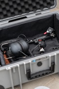 A protective case is open to reveal various audio-visual equipment inside. It includes headphones, a gimbal, and other accessories arranged neatly. The interior of the case is lined with foam padding for protection.