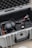 A protective case is open to reveal various audio-visual equipment inside. It includes headphones, a gimbal, and other accessories arranged neatly. The interior of the case is lined with foam padding for protection.