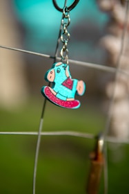 A vibrant gift-style keychain hanging from a colorful backpack strap outdoors.