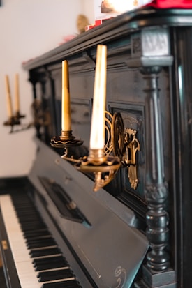 A vintage upright piano with ornate candle holders and candles mounted on its dark wooden body. The piano keys are partly visible, and the intricate design suggests an antique style.