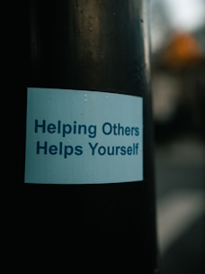 a sticker on a pole that says helping others helps yourself