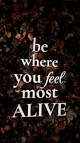 Bold, white text with the motivational message 'be where you feel most ALIVE' is overlaying a background of dark, leafy foliage. The leaves are predominantly dark green with earthy brown and muted red tones, contributing to a natural and organic look.