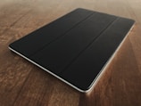 Person examining a tablet device on a wooden table.