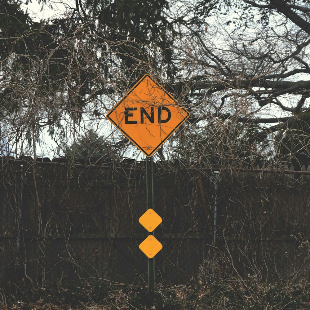 a yellow end sign sitting next to a wooden fence