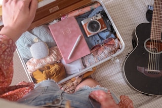 a person looking at a packed bag next to a guitar