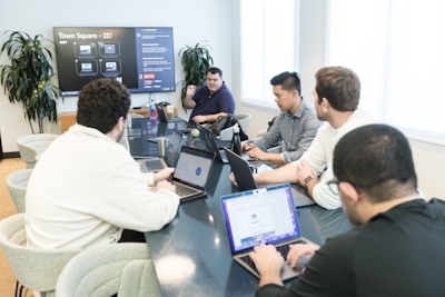 a group of men sitting around a table with laptops