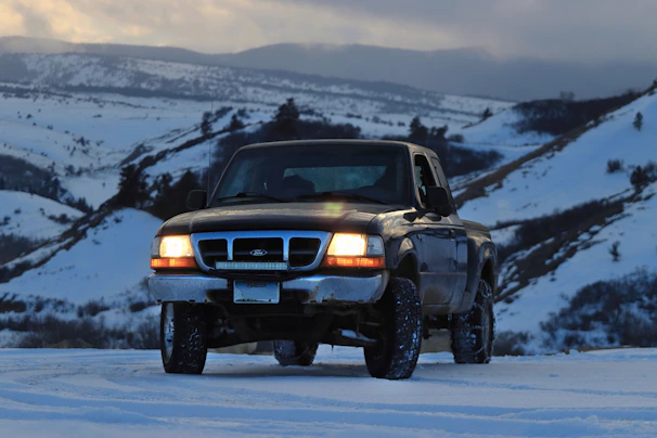 A rugged pickup truck being carefully loaded onto an open auto transport carrier at dawn.