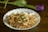 A white dish filled with cooked cabbage garnished with fresh herbs and topped with a dollop of sour cream, placed on a wooden surface. In the background, a purple tulip with a green stem lies horizontally.