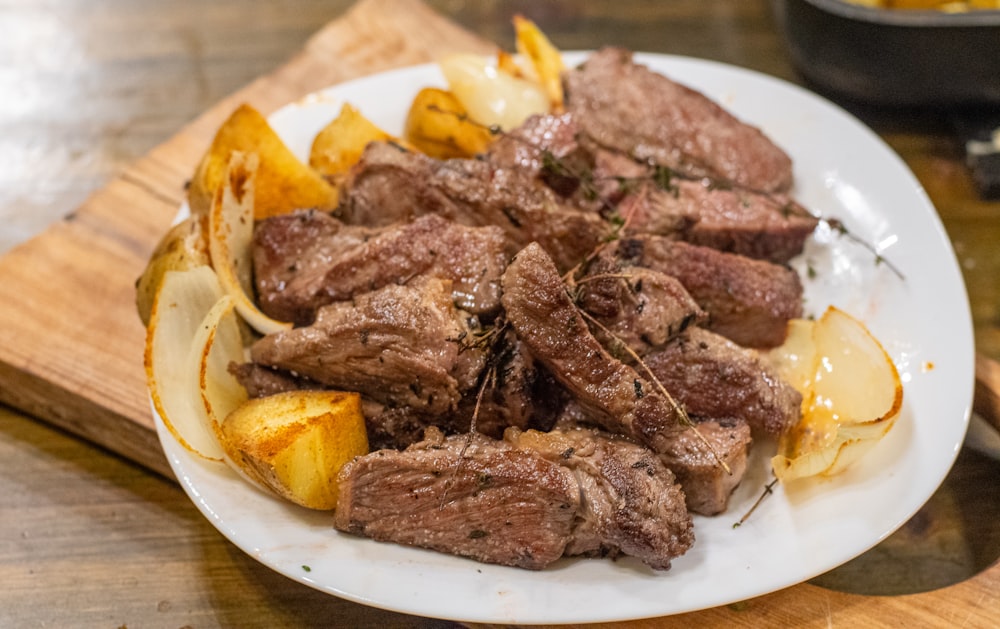 un plato blanco cubierto con bistec y patatas