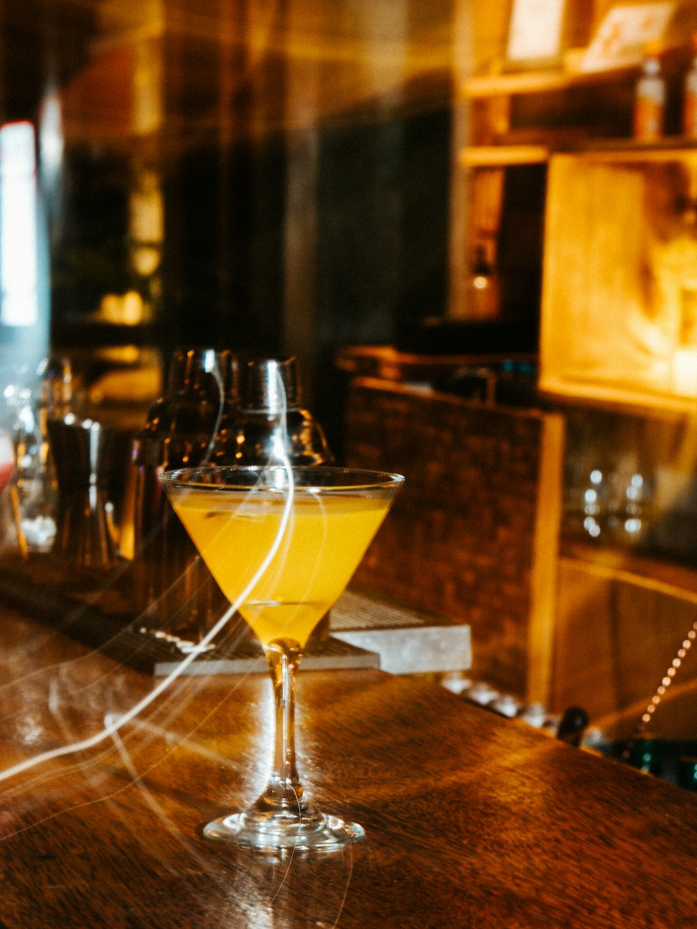 a glass of yellow liquid sitting on top of a wooden table