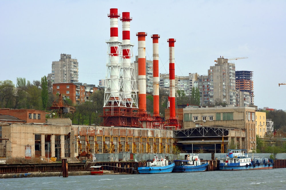a large factory with red and white pipes next to a body of water