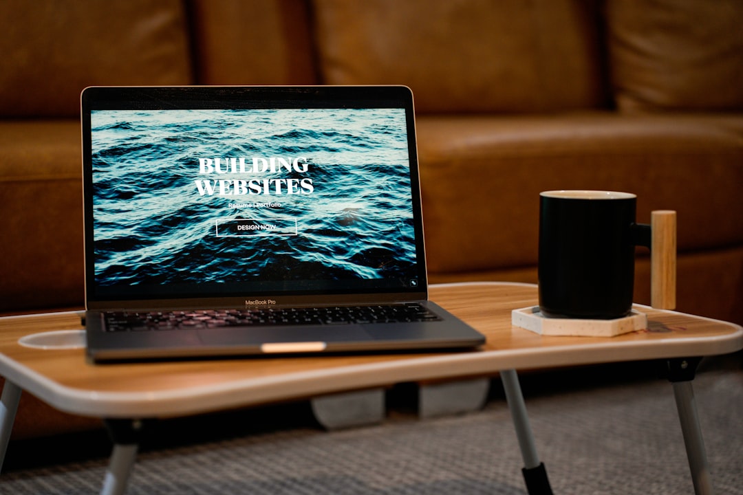 a laptop computer sitting on top of a wooden table, A laptop, MacBook, on top of a portable table with coffee tea mug on the side.