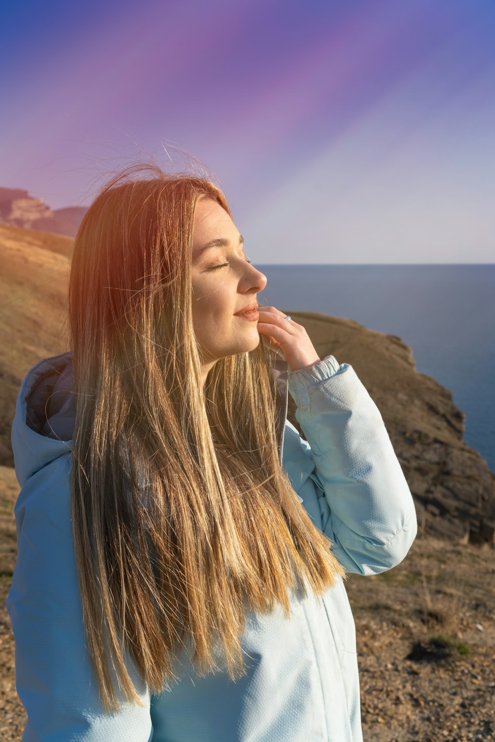 a woman standing on top of a rocky hill next to the ocean