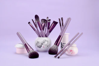 a white vase filled with purple makeup brushes