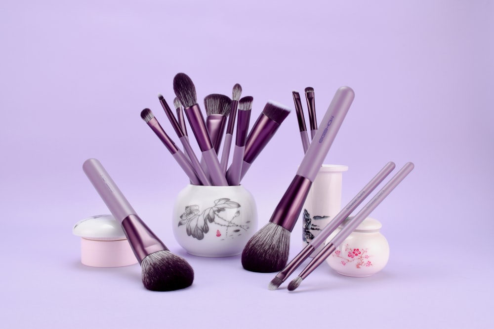 a white vase filled with purple makeup brushes