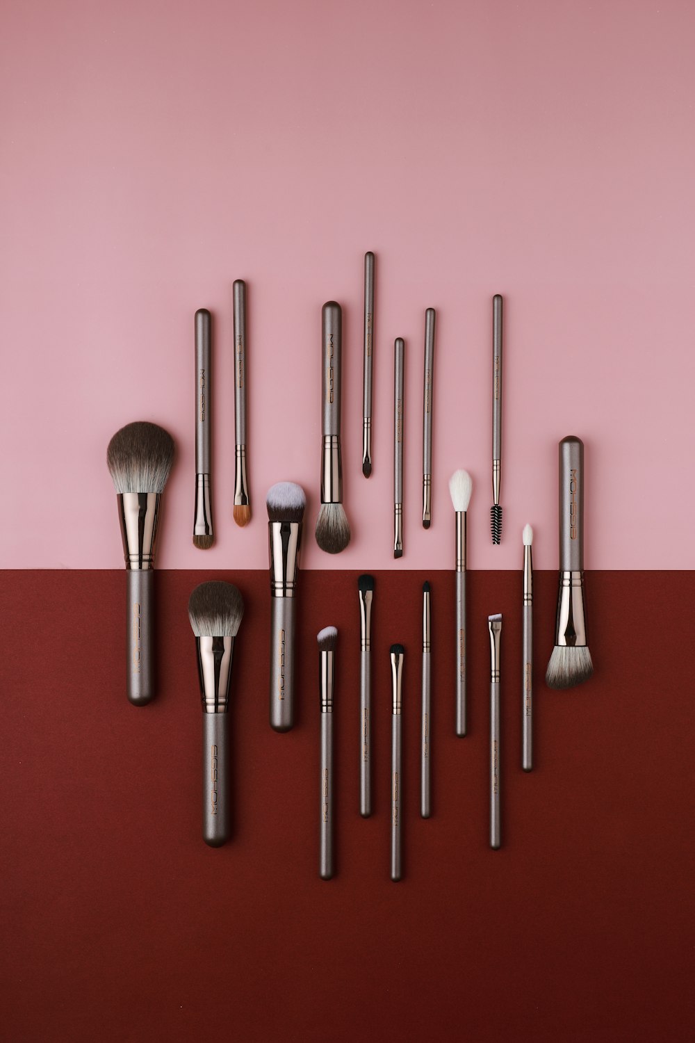a collection of makeup brushes on a pink and red background