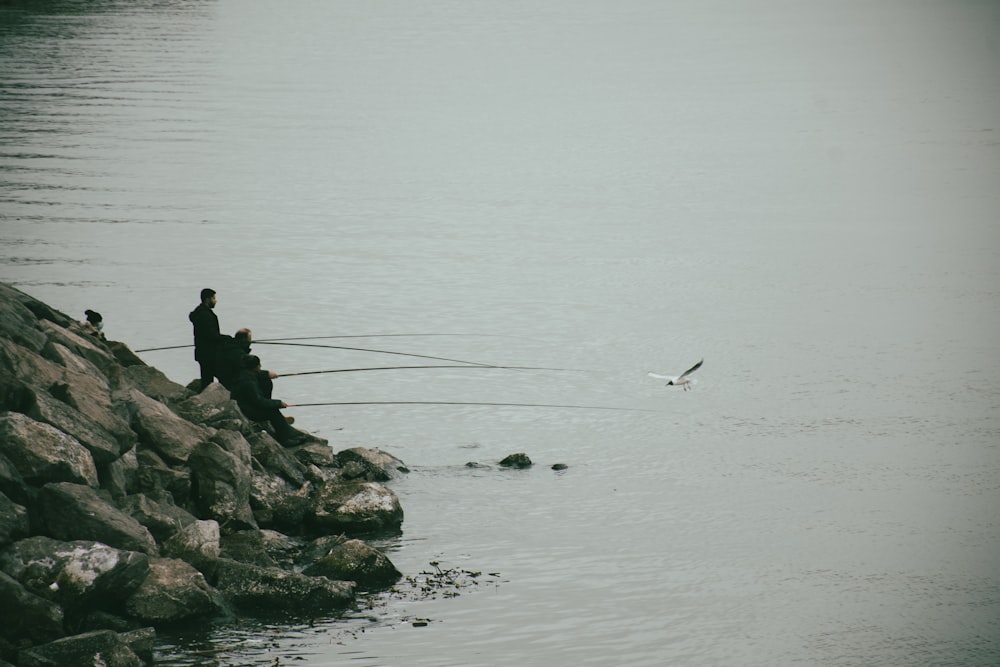 a couple of people sitting on top of a rock next to a body of water