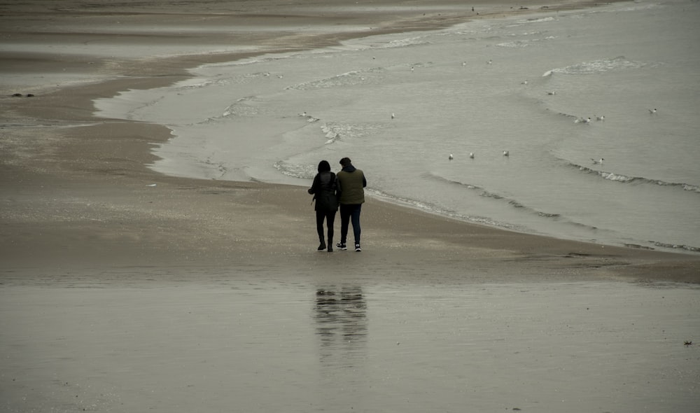 two people walking on a beach next to the ocean