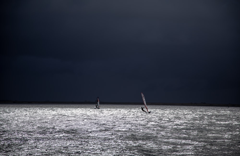 two windsurfers in the ocean under a dark sky