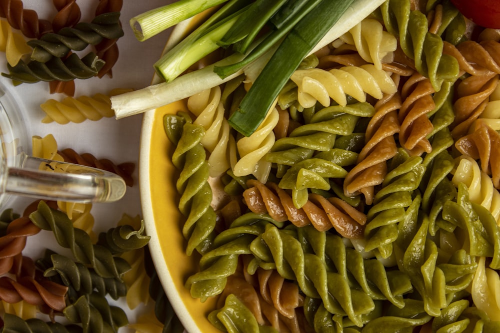 a yellow bowl filled with pasta and vegetables