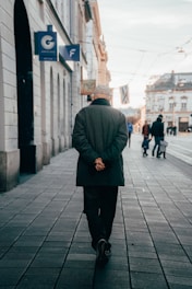 Man wearing a sleek jacket walking down a city street at sunset