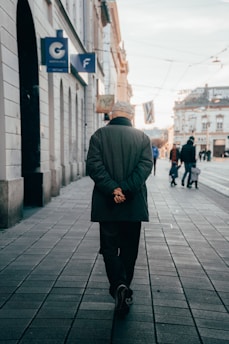 Man wearing a sleek jacket walking down a city street at sunset