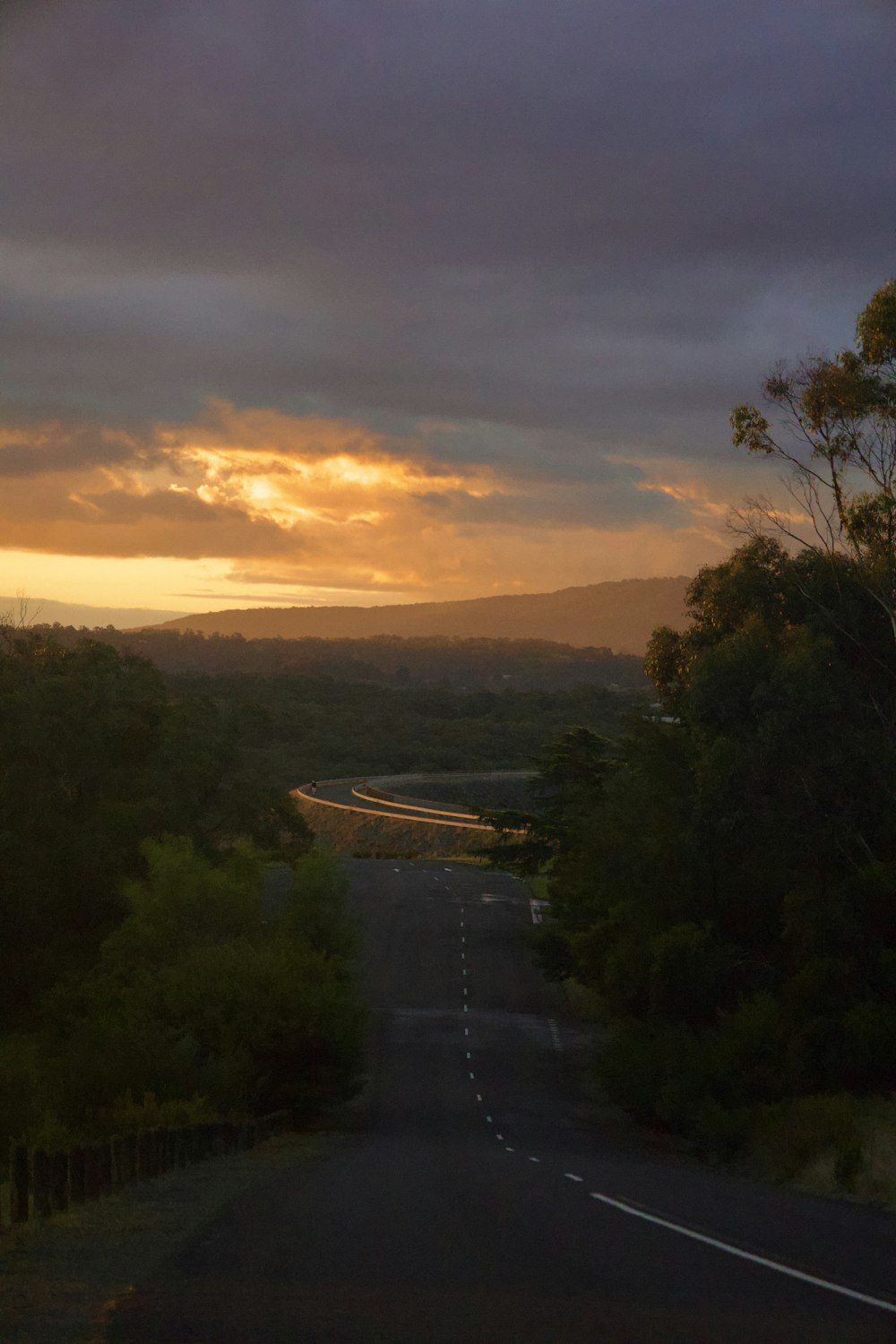 the sun is setting over a road in the middle of the forest