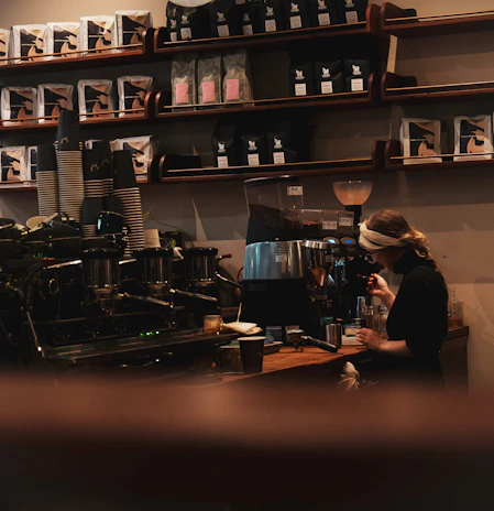 Friendly barista pouring freshly brewed coffee into a ceramic mug, with bags of Roastoria coffee in the background.