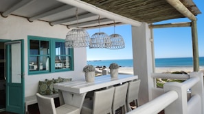 Dining area showcasing timeless coastal cottage style with soft neutrals, vintage rugs, and organic textures blending indoors and out.