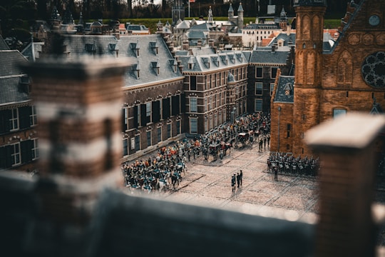 A miniature cityscape featuring detailed scale models of historic buildings, with brick and slate roofing. The scene shows a gathering of tiny figures, some in formation resembling a parade or guard ceremony, with a sense of historical architectural style.