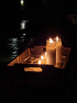 A rustic wooden tray holding several small votive candles surrounded by eucalyptus leaves.