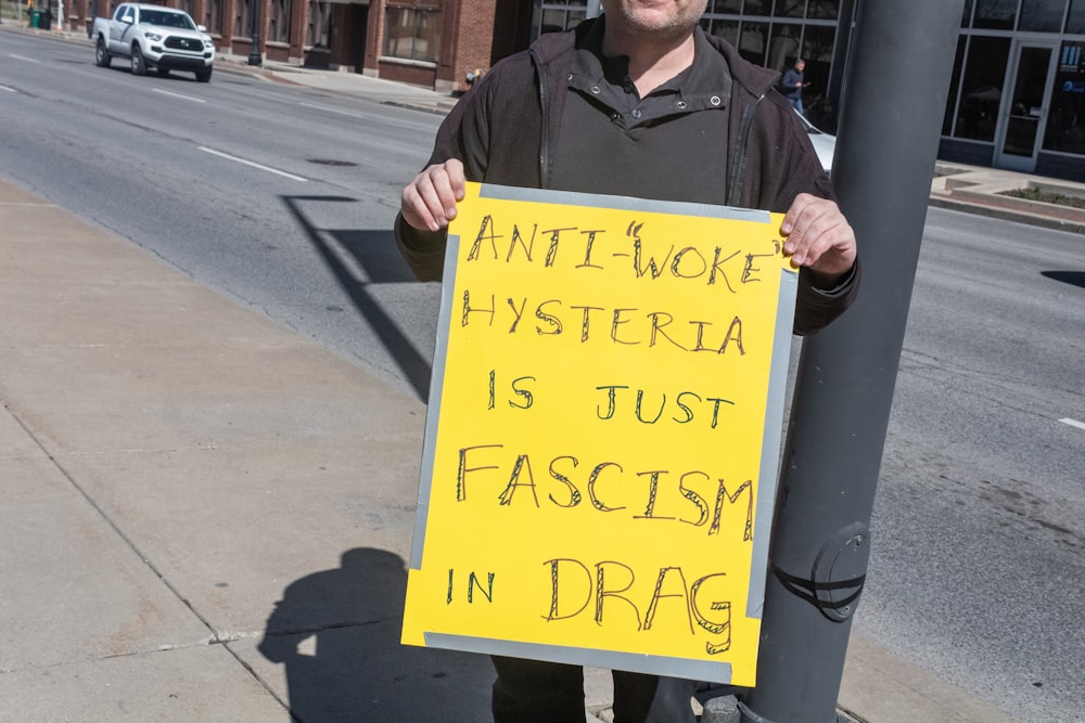 a man holding a sign that says anti - more hyperia is just fasc