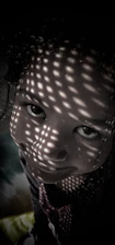 A child's face is partially illuminated with patterned light, creating a playful and mysterious atmosphere. The lighting pattern consists of evenly spaced dots that cover the face, resulting in a captivating visual effect.