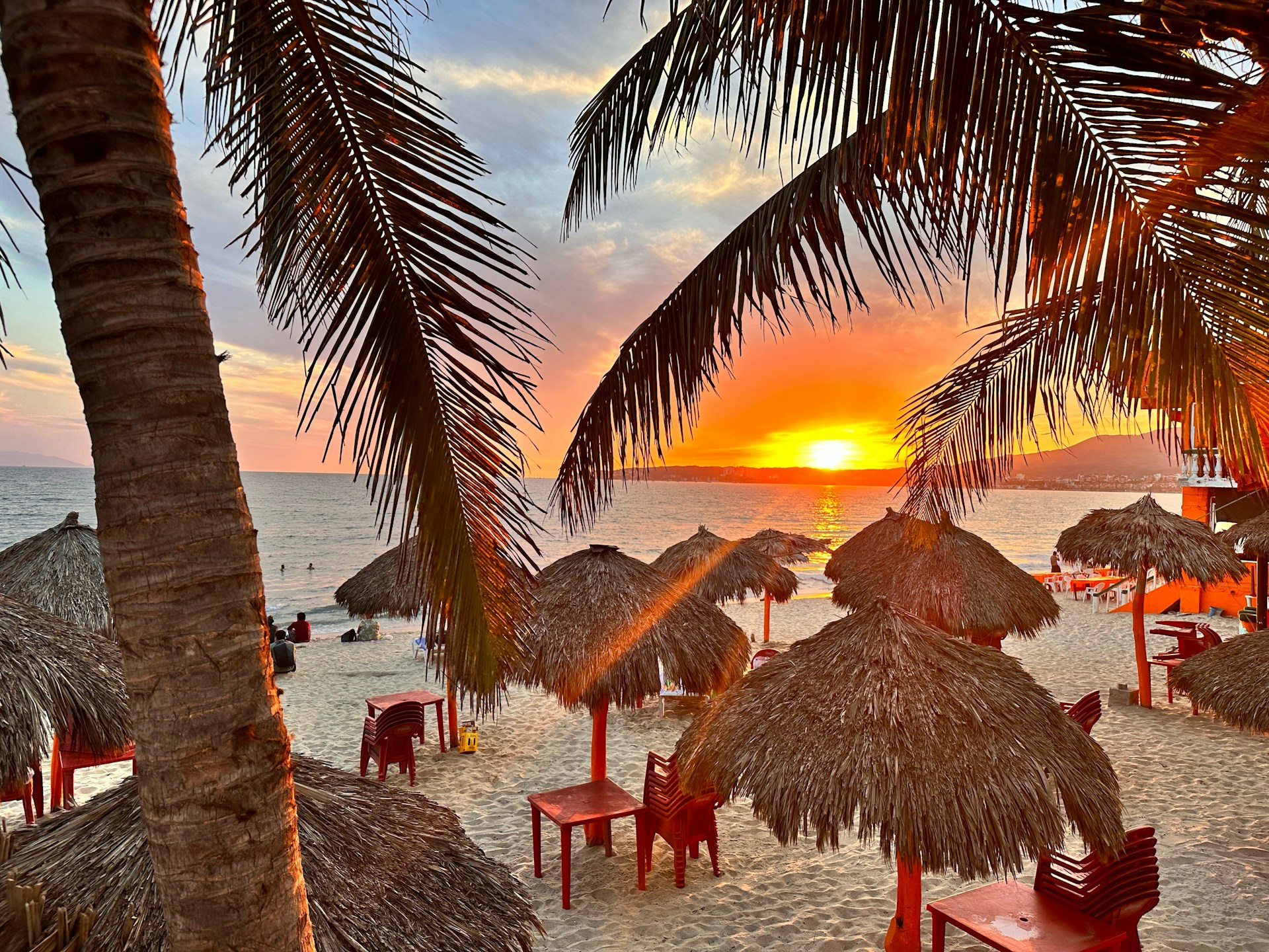 A vibrant beach scene at sunset highlighting a special last-minute getaway offer with colorful umbrellas and calm waves.
