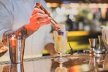A bartender placing a large clear ice cube into a stylish cocktail glass.