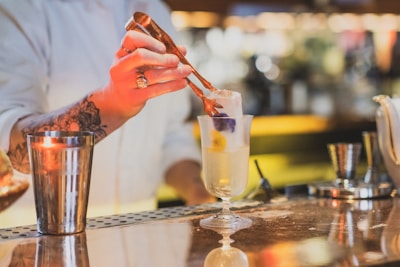 A bartender placing a large clear ice cube into a stylish cocktail glass.