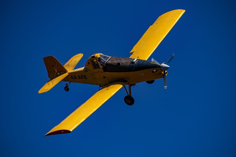 a small yellow airplane flying through a blue sky