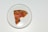 A slice of pizza on a round white plate with a thin crust. The pizza has pepperoni, tomato sauce, and fresh basil leaves.
