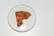 A slice of pizza on a round white plate with a thin crust. The pizza has pepperoni, tomato sauce, and fresh basil leaves.
